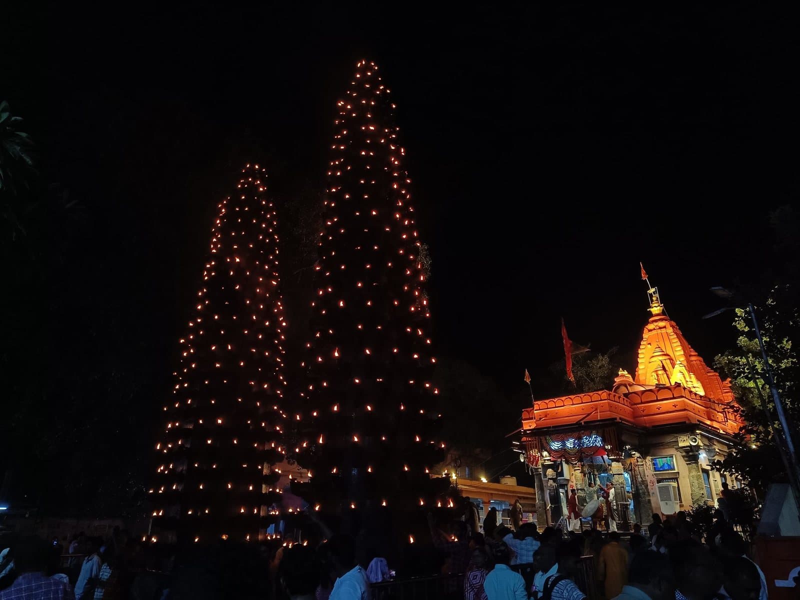 रात्रि में दीपस्तम्भों पर प्रज्वलित सहस्रों दीप, दाहिनी ओर प्रकाशित मन्दिर-शिखर एवं श्रद्धालुओं की भीड़